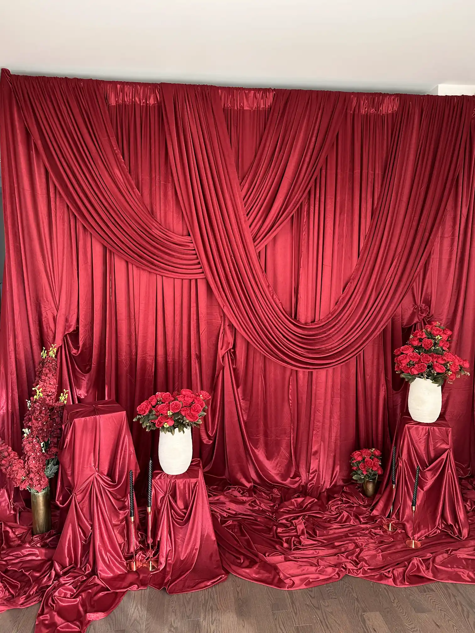 Burgundy satin drape backdrop with crossed swag draping, red rose arrangements and fabric-covered pedestals