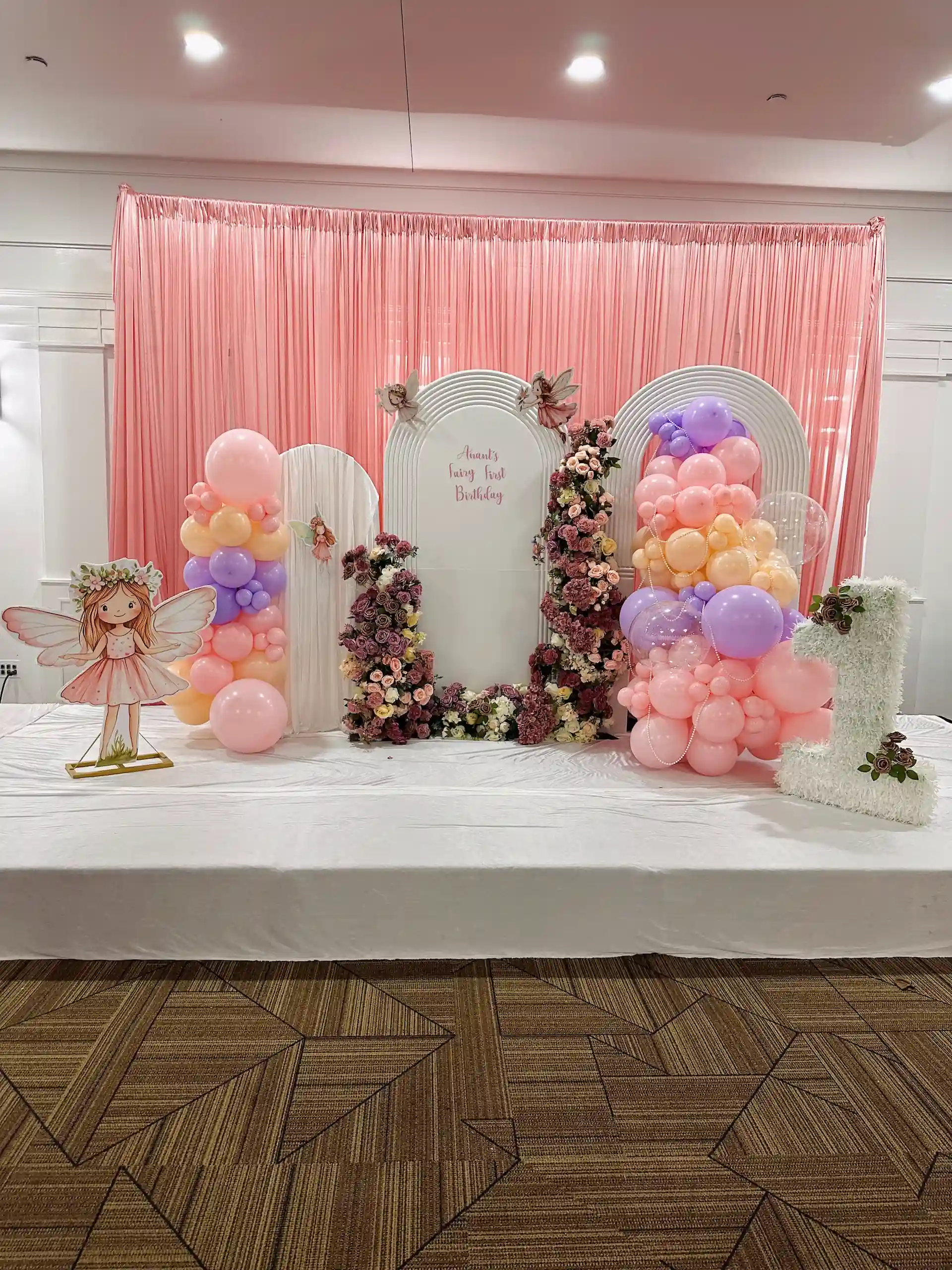 Fairy-themed first birthday balloon backdrop with pastel balloon columns and pink draping